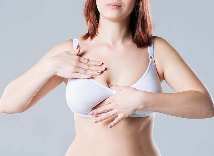 Woman in white bra examining her breasts
