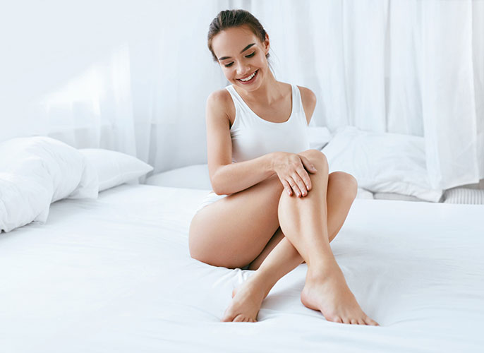Woman sitting on her bed and feeling her smooth legs
